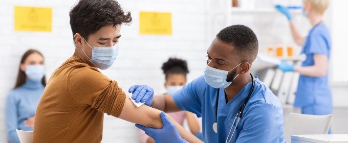 A male nurse wipes the arm of a young man who is about to receive a vaccination