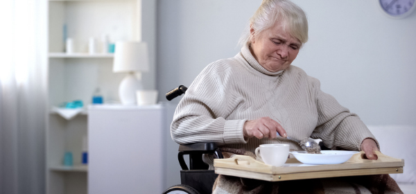 Middle-aged woman in a wheel chair and eats a meal alone.