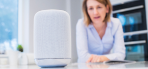 Picture of smart speaker on couter with woman leaning towards it in the background.