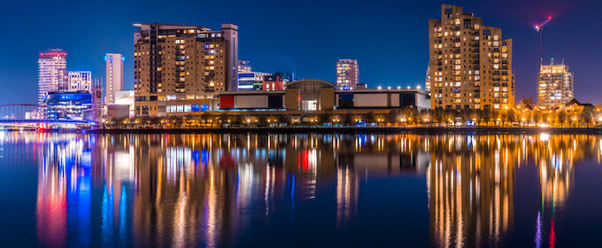 Image of media city in Salford lit up at night reflected in the water of the quay