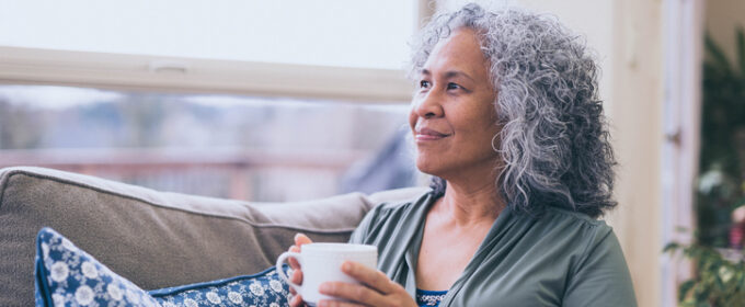 Woman of colour drinking a cup of tea and looking out the window