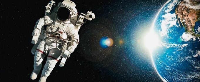 An astronaut floating in space with the Sun and Earth pictured behind them