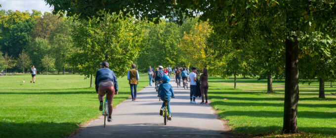 Image of a path through a green park with a few people walking and cycling through it.
