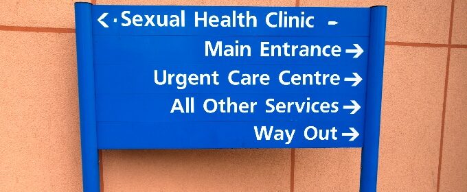 A directory sign at an NHS facility; one arrow points to the sexual health clinic