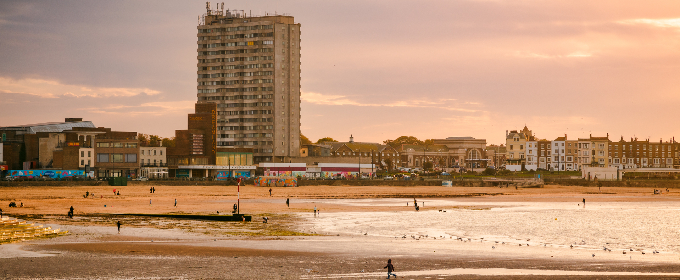 The beach at Margate, in Kent, at sunset. In the background, a tower block stands behind the Dreamland theme park.