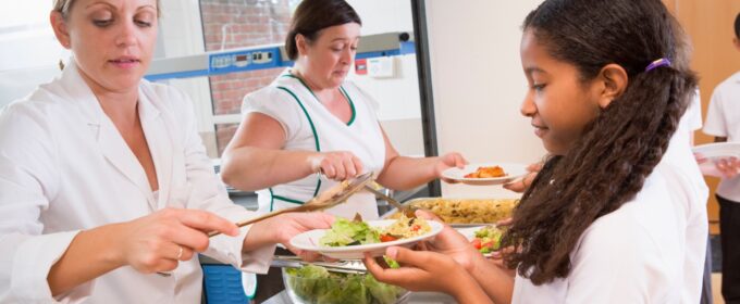 Child is served a nutritious school meal by smiling dinner ladies