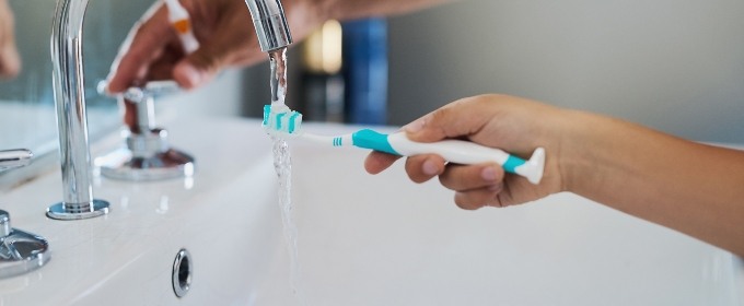 A child's hand holding a toothbrush under a running tap.