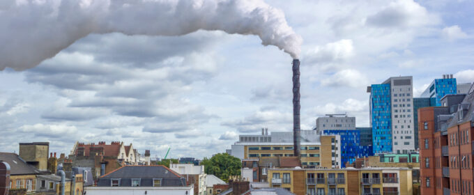 Industrial chimney pluming out smoke surrounded by an urban landscape of buildings.