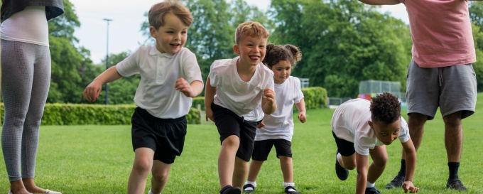 Four children in white t-shirt uniforms are smiling and running