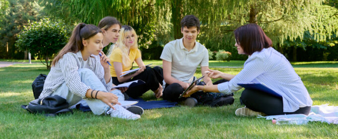 Article image. Outdoor, group of students with female teacher sitting on grass