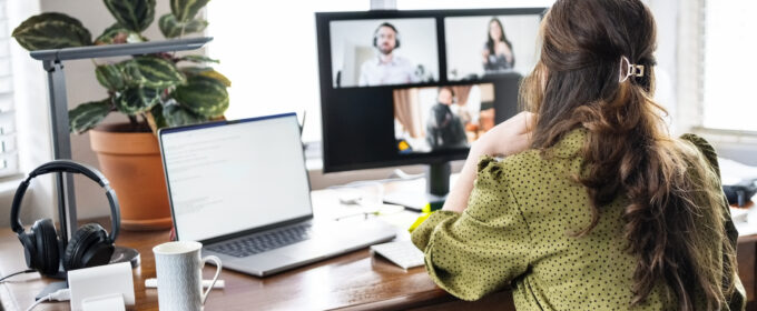 Women working from a home office, looking at a monitor, with laptop open to her left.
