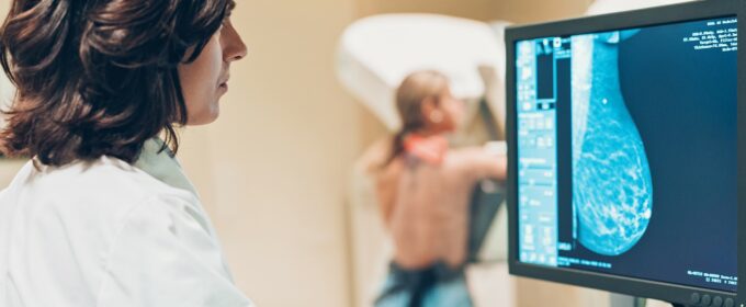 Image of woman getting a mammogram with a medical professional looking at the scan