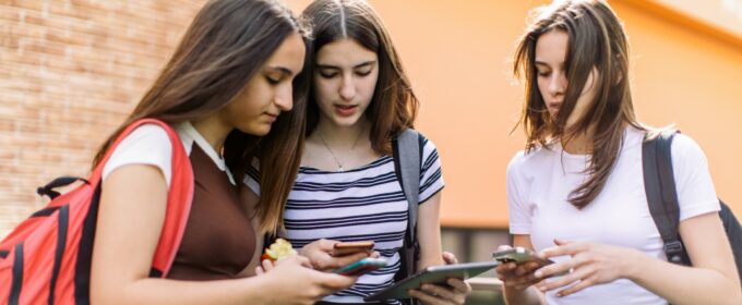 Three teenage girls standing together talking whilst looking at their phones