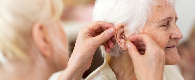 A female healthcare assistant fits a hearing aid for an older woman.