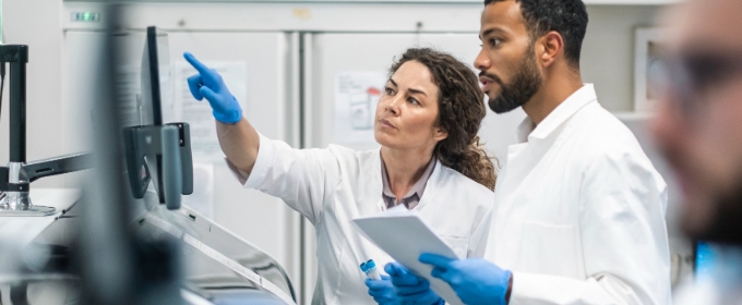 Two researchers, one man and one woman, discuss data on a computer screen in a laboratory.