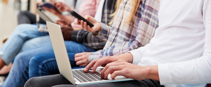 Image of young people sitting in a row on their phones and laptops