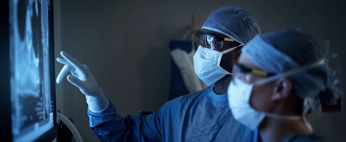 Two surgeons in scrubs looking at a scan on an electronic screen.