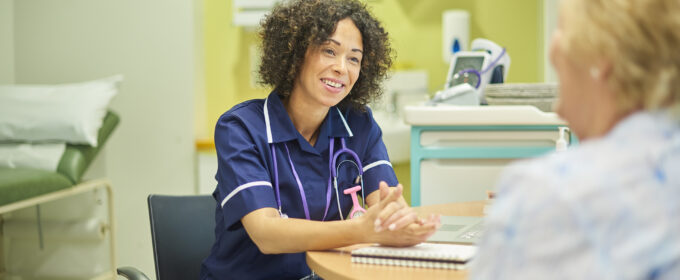 A smiling medical professional chatting with an older female patient in an examination room.