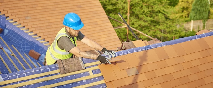 A builder on the roof of a British house on a sunny day, changing the tiles.