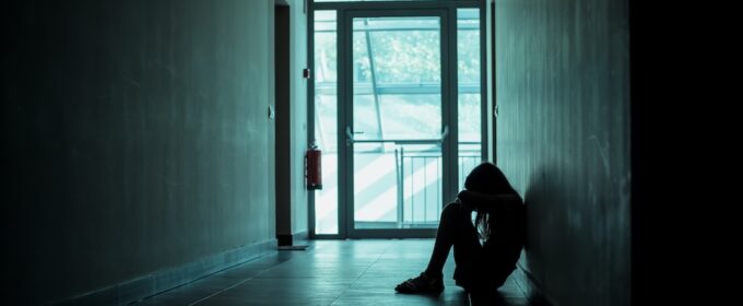 Child on sitting on floor in dark corridor, head in hands.